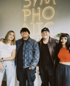 Four team members stand together in front of a wall with "SYMPHONIC" in neon lights, posing for a group photo.